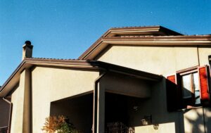 Clogged rain gutter filled with pine needles on a Northwest-style home under tall evergreen trees.