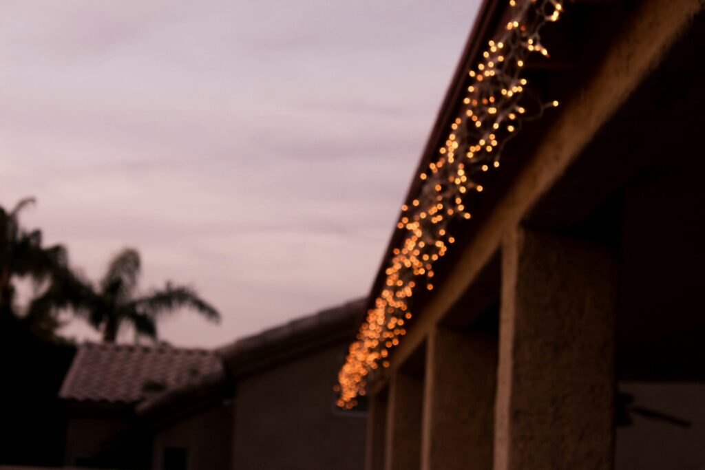 Alt Text: Homeowner safely hanging Christmas lights along a Medford, Oregon roofline using gutter clips, following HomeMasters’ roof protection and safety tips for the holiday season.