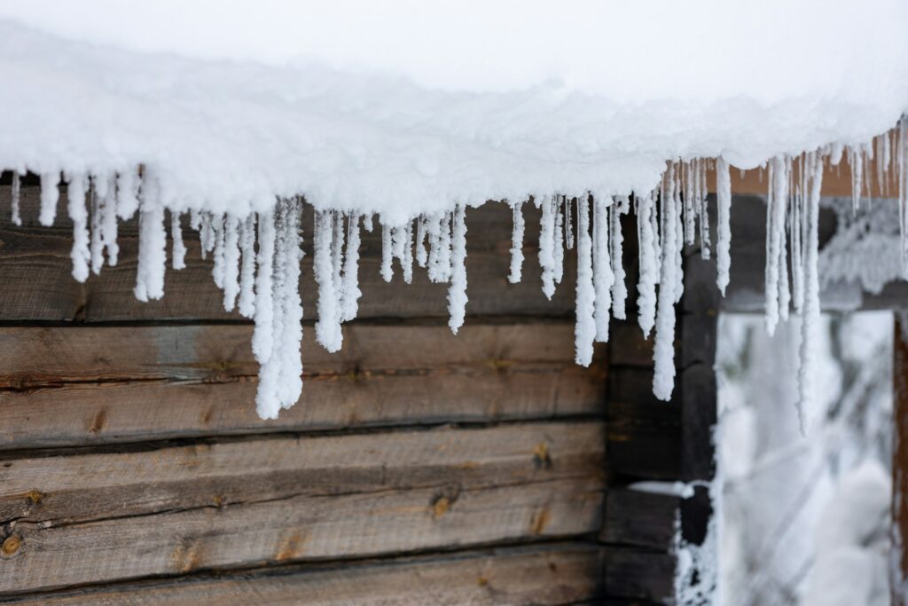 Ice dams forming on roof eaves in Bend Oregon winter with heavy snow accumulation on residential home