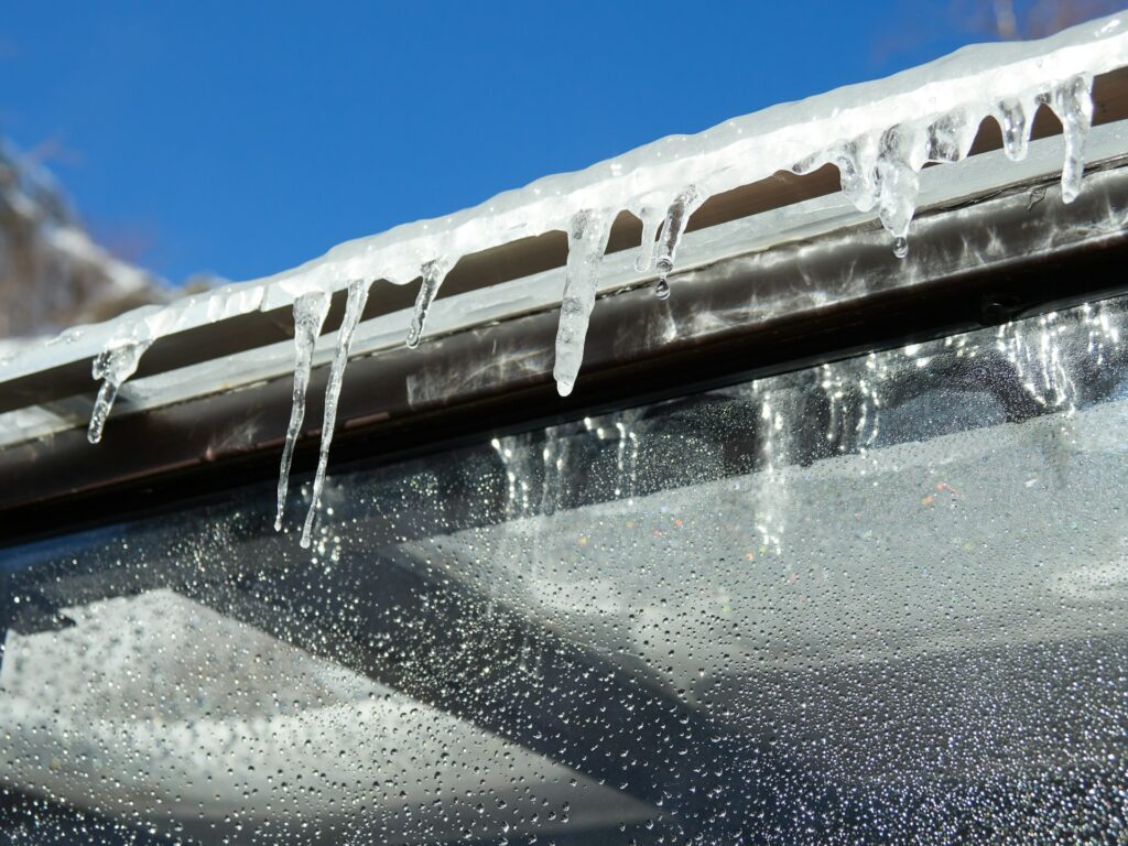 Icicles and ice dams on Southern Oregon home roof in Ashland with snow-covered mountains visible