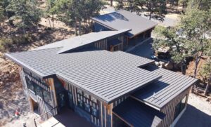 Dark standing seam metal roof on a modern home among pine trees, ember resistant roofing by HOMEMASTERS Bend for Sisters