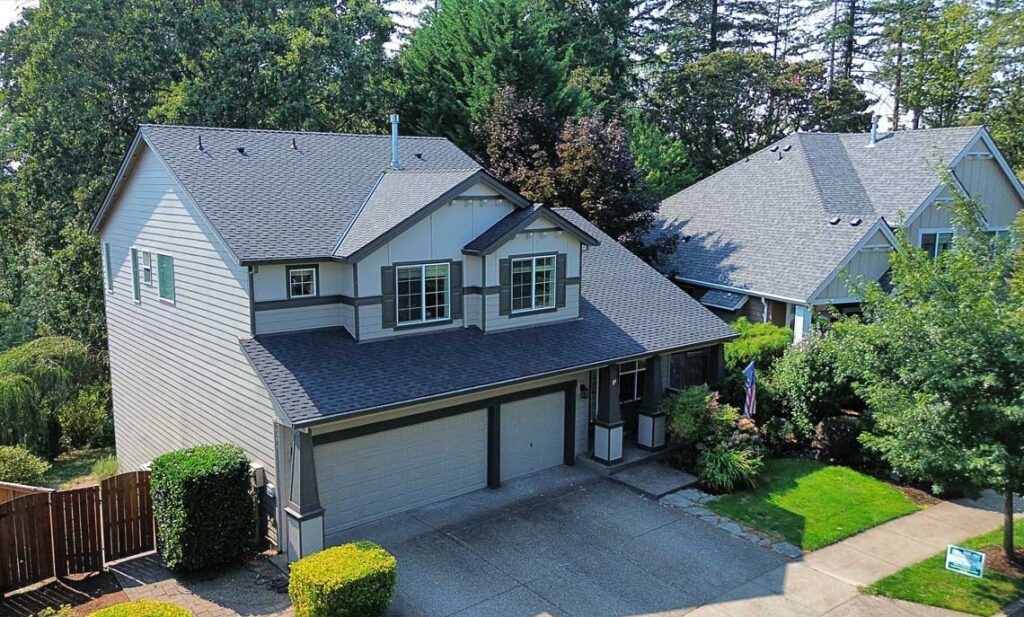 Seamless gutters along a new gray shingle roof beneath tall firs, gutter guards by HOMEMASTERS Portland East for Sandy