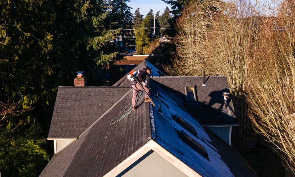 Crew member applying roof moss treatment with a backpack sprayer on asphalt shingles, HOMEMASTERS service in Sherwood
