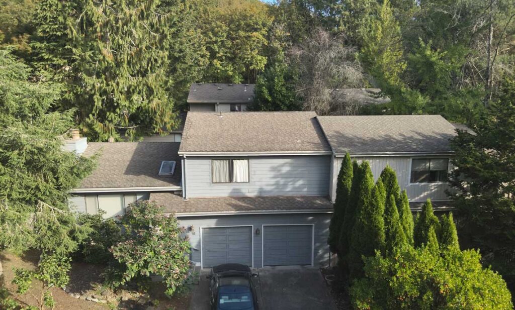 Two story home with gray lap siding, trim and a dark shingle roof among tall firs, siding replacement guidance for Woodburn