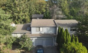 Two story home with gray lap siding, trim and a dark shingle roof among tall firs, siding replacement guidance for Woodburn